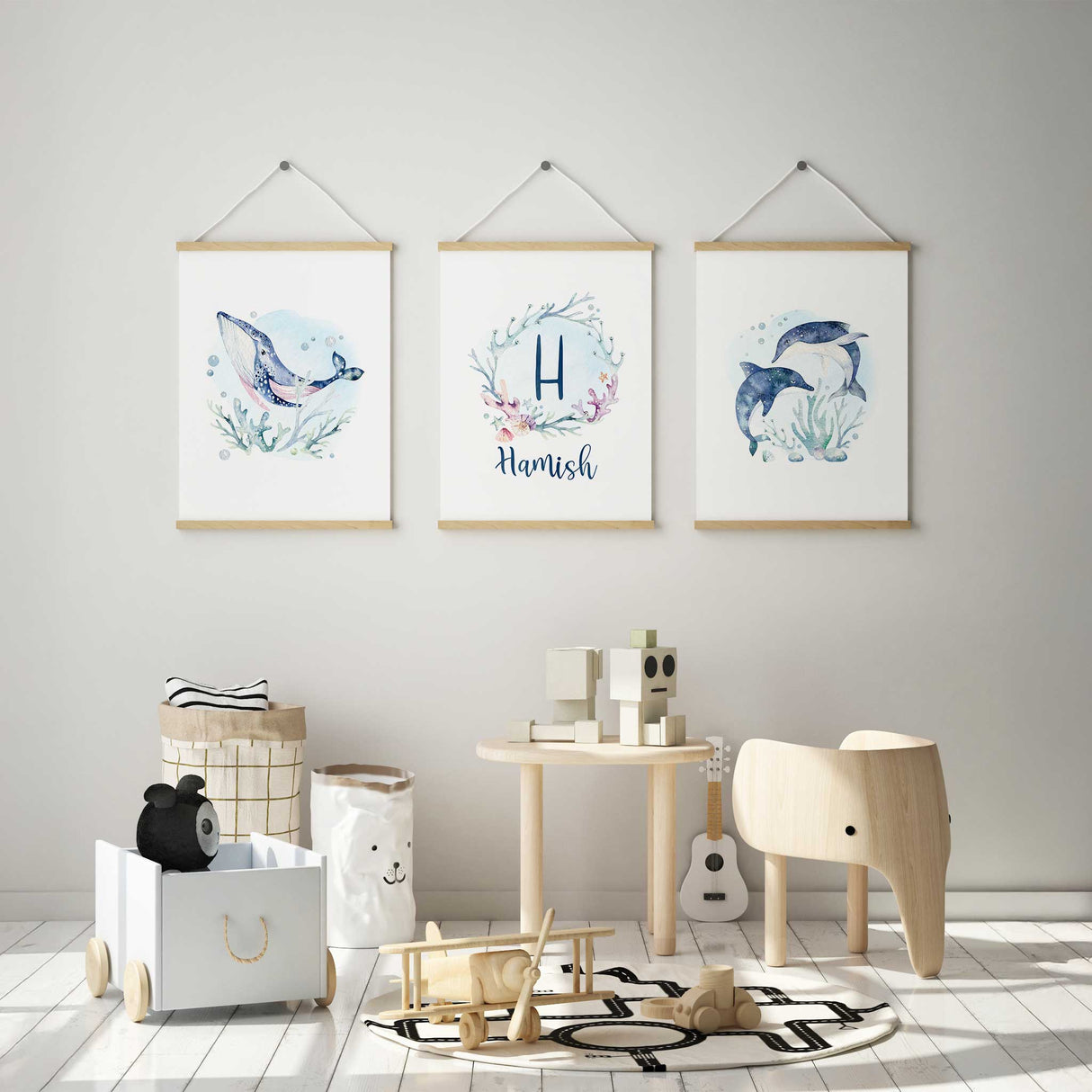Detailed view of three delicate watercolor paintings showcasing marine life, including dolphins, a whale, and a personalized coral wreath, in a harmonious ocean theme.