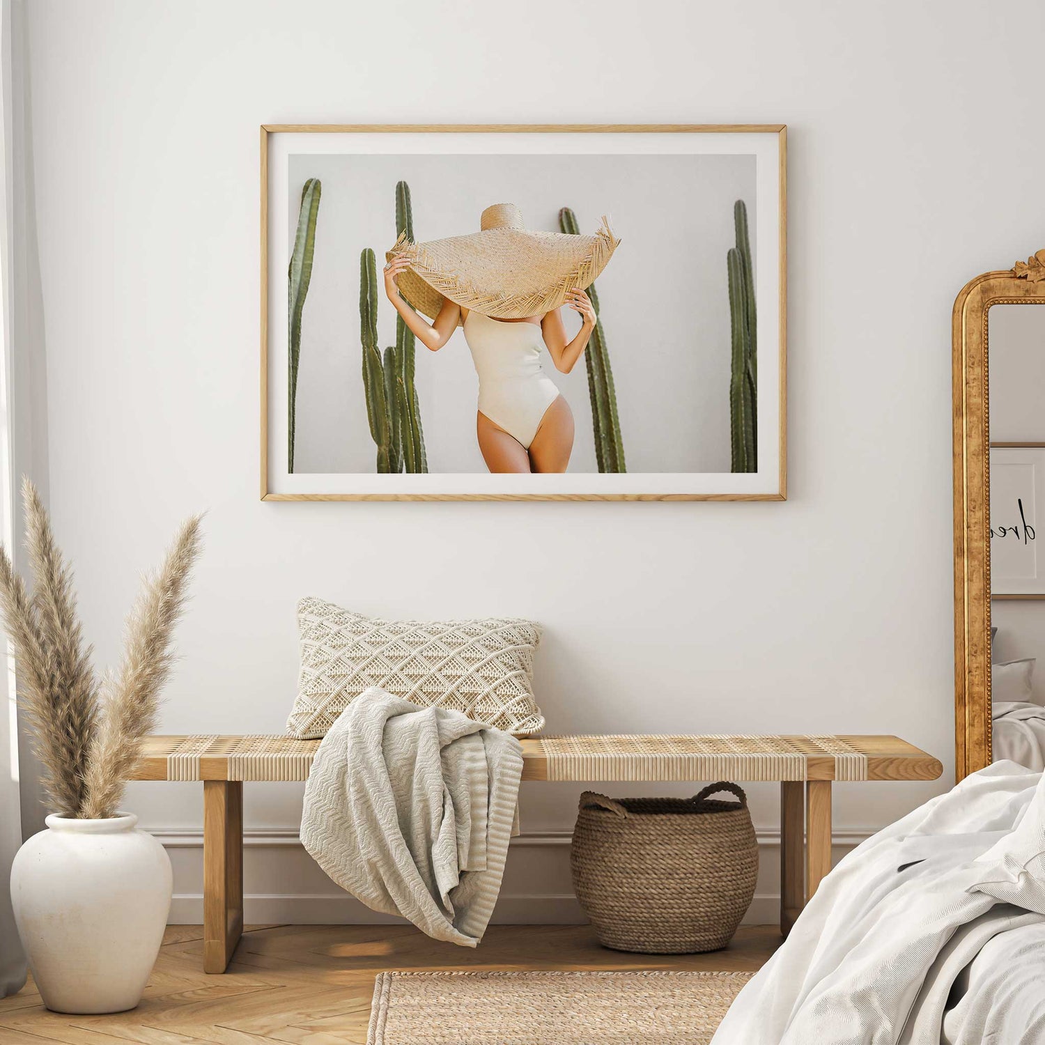 Minimalist wall art of a woman in neutral swimsuit with oversized straw hat, surrounded by tall green cacti.
