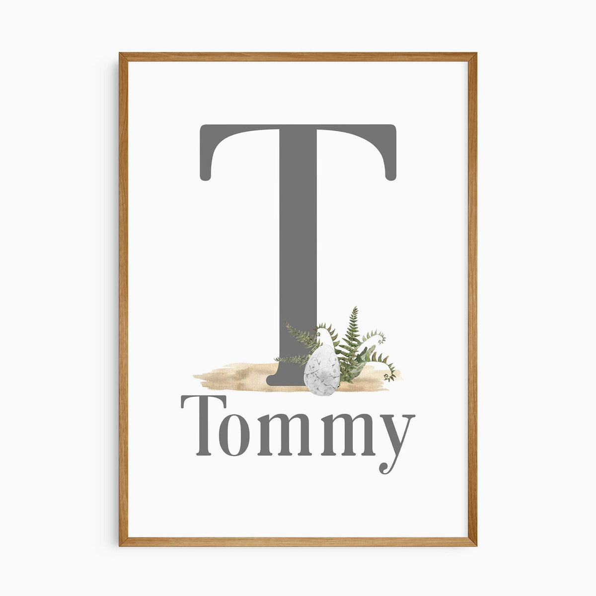 Personalised dinosaur initial print with a large grey initial, and childs' name, a dinosaur egg and green fern details.