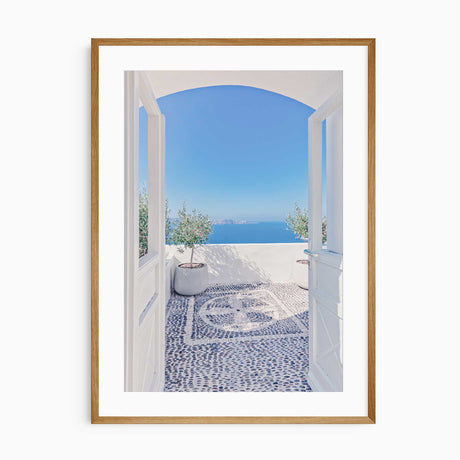 A beautiful patio overlooking the blue sea with an elegant white archway, stone mosaic floor, and potted olive trees in Santorini, Greece