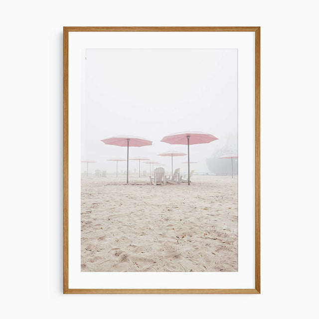 Minimalist beach wall art featuring pink umbrellas and wooden chairs on soft sand