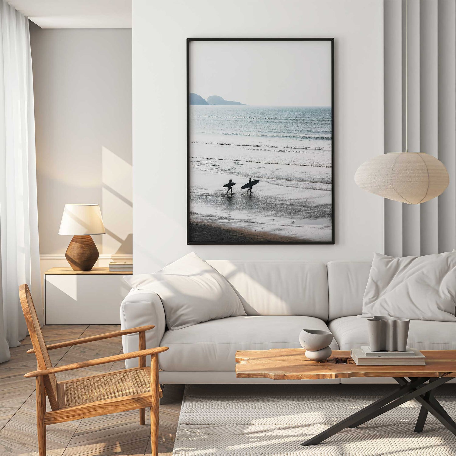 Two surfers walking along a quiet beach shoreline carrying surfboards with gentle ocean waves in the background.