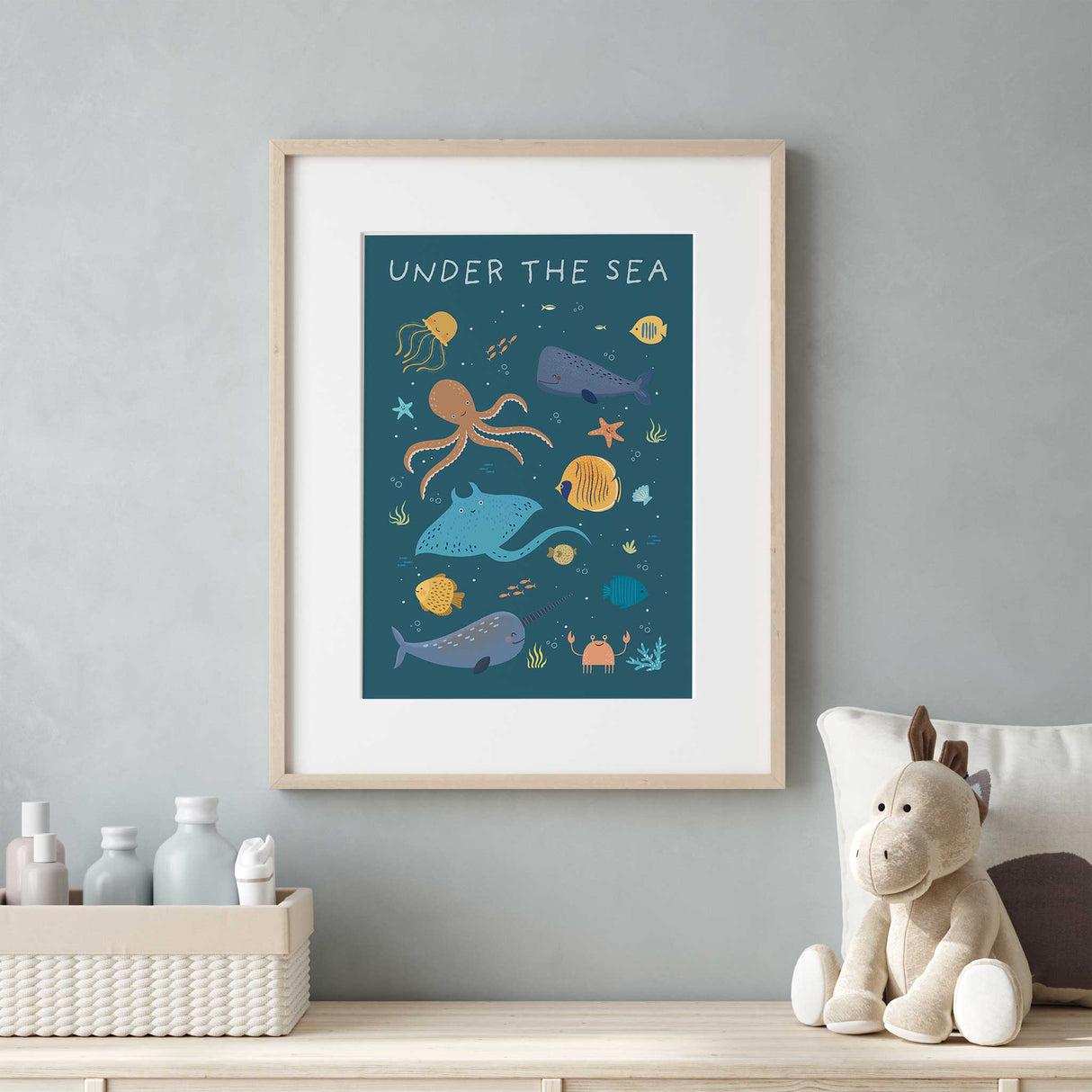 A charming ocean-themed print with happy marine animals, including a jellyfish, starfish, and different types of fish, all floating in a dark blue sea. The text UNDER THE SEA is written in a playful hand-drawn font