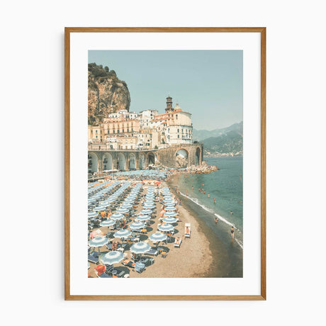 Artwork of a coastal scene with buildings, beach, and umbrellas.
