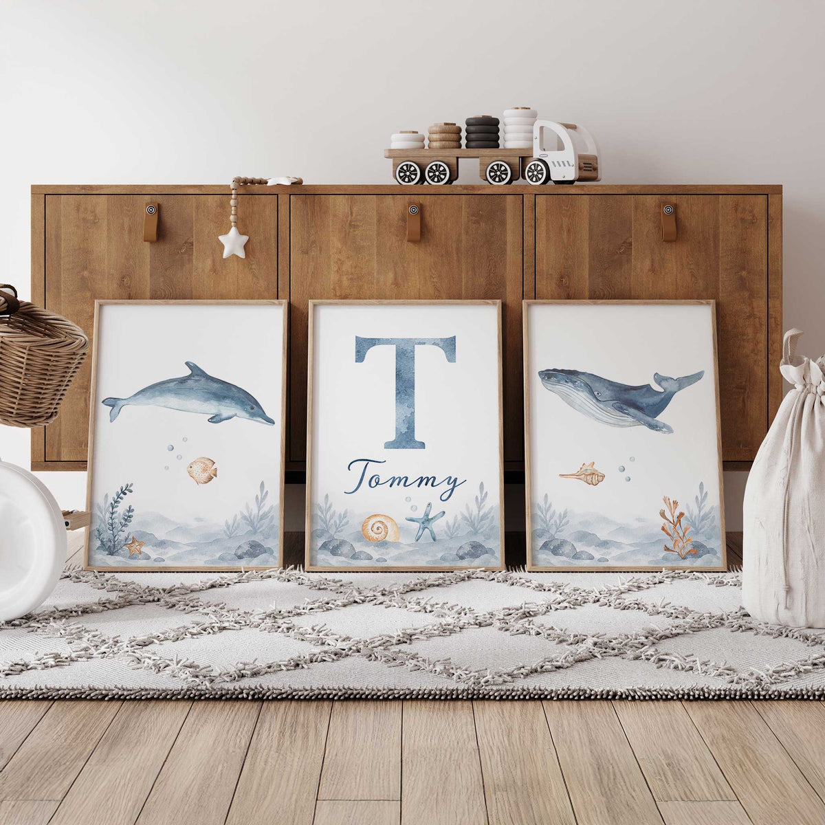 Three watercolour ocean prints with a dolphin, whale and personalised initial and name above a soft blue rocky seabed.