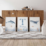 Three watercolour ocean prints with a dolphin, whale and personalised initial and name above a soft blue rocky seabed.