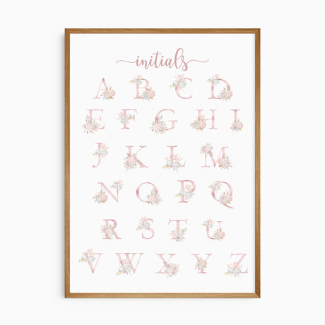 Close-up of a blush pink floral initial with soft pastel flowers, grey leaves and gold-style details.