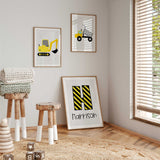 Construction print set with a yellow excavator, dump truck and striped letter above name on light grey with white borders.