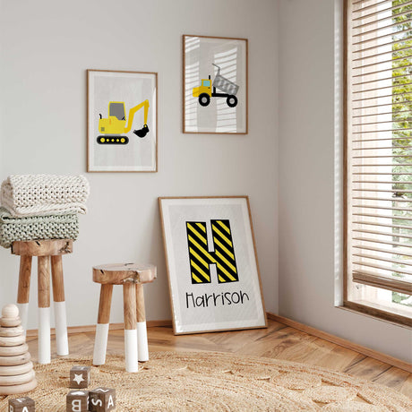 Construction print set with a yellow excavator, dump truck and striped letter above name on light grey with white borders.
