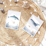 Blue watercolour dolphin and whale prints with a sandy fish, shells, starfish and coral above matching seabed scenes.