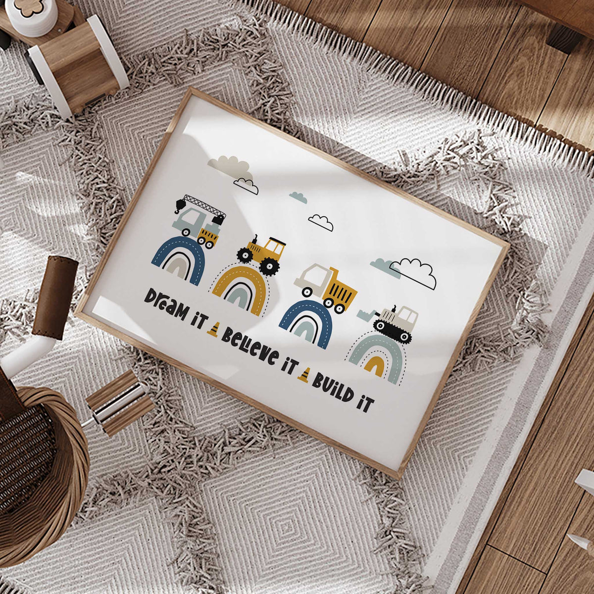Dream It Believe It Build It print with four building vehicles on navy, mustard and aqua rainbows beneath clouds.