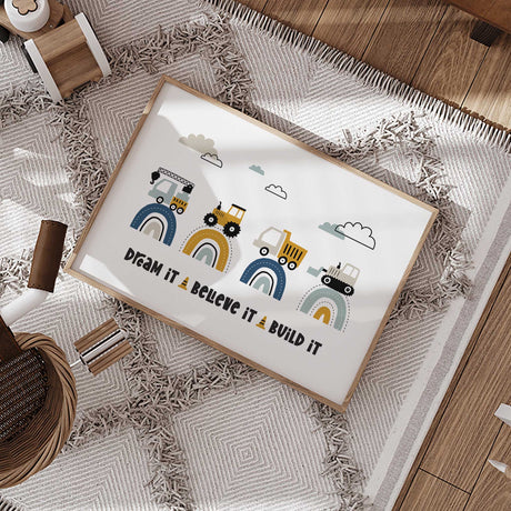 Dream It Believe It Build It print with four building vehicles on navy, mustard and aqua rainbows beneath clouds.