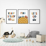 Car wall art set with personalised name on a mustard road print, flanked by Ready Steady Go and Let's Go designs with cars.