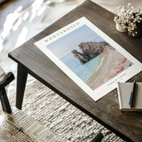 Monterosso beach photography print with turquoise sea, rock formations, striped parasols and a white border.