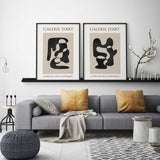 Two neutral abstract prints featuring bold black curves on warm beige panels with Galerie d’Art lettering above.