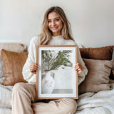 Neutral tone artwork featuring olive stems in a white ceramic pot vase