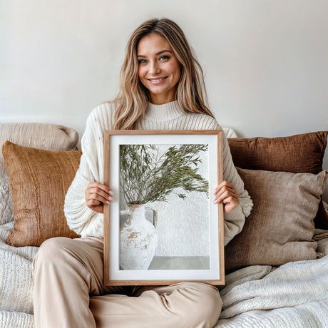 Neutral tone artwork featuring olive stems in a white ceramic pot vase