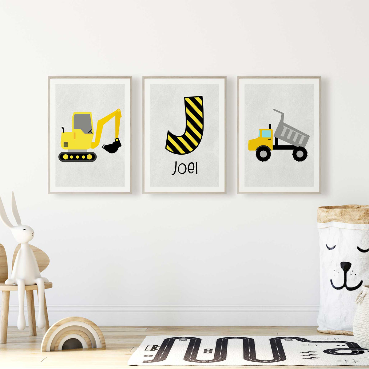 Three personalised construction prints with a yellow digger, dump truck and black and yellow striped initial above name.
