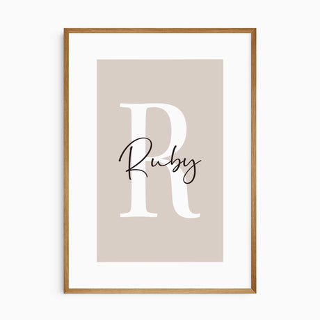 Personalised name print with a large white initial and black script lettering on a warm pink background.