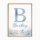 Personalised ocean name print with a blue watercolour initial and name lettering above a shell, starfish and rocky seabed.
