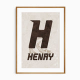 Personalised name print with a dark brown racing-style initial, uppercase name and beige tyre tracks on a beige background.