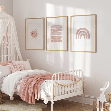 Three pink wall art prints featuring a smiling sun, rainbow and personalised affirmations.