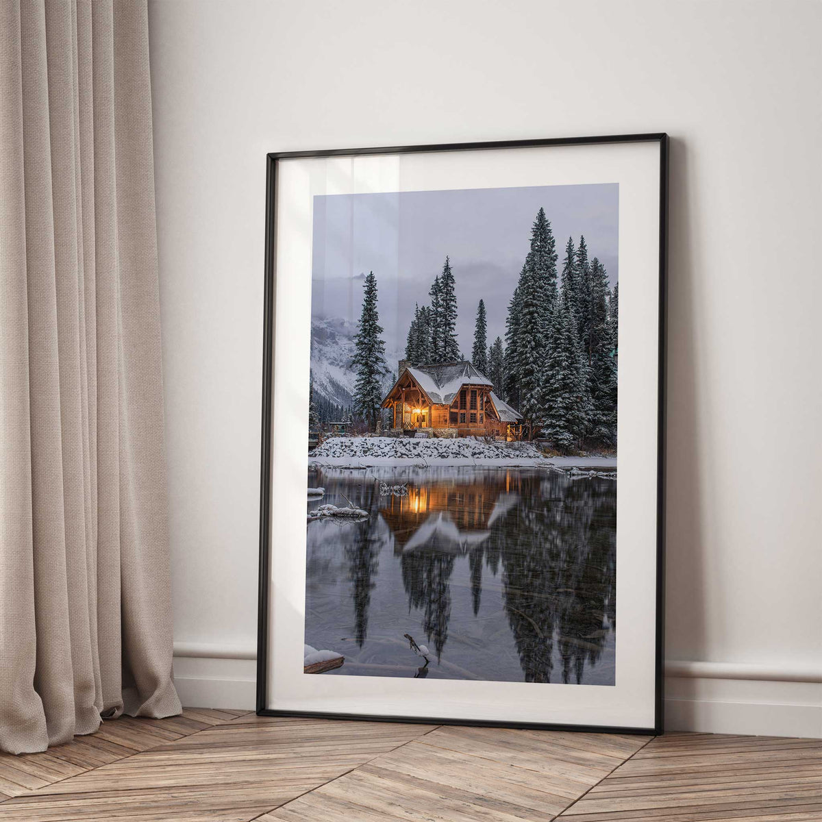 Snowy lake cabin wall art with warm window lights, tall fir trees and their reflection in the dark water.