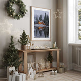 Winter cabin wall art showing warm lights reflected in a snowy lake, with pine trees and an even white border.