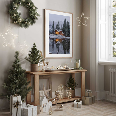Winter cabin wall art showing warm lights reflected in a snowy lake, with pine trees and an even white border.