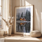 Winter landscape print featuring a lit lakeside cabin, snow-covered trees and a reflection across still water.